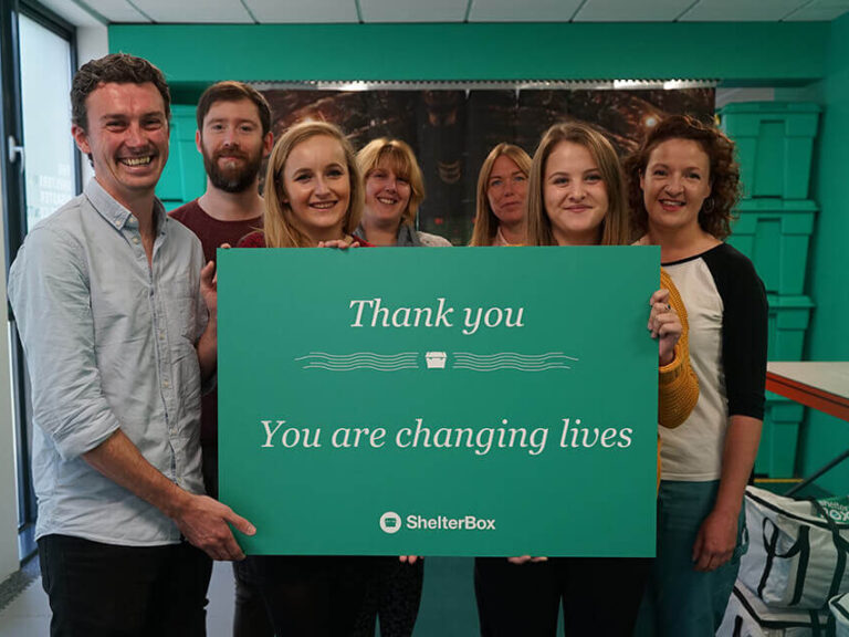 ShelterBox Supporter Care Team holding a green board that says Thank you, you are changing lives.