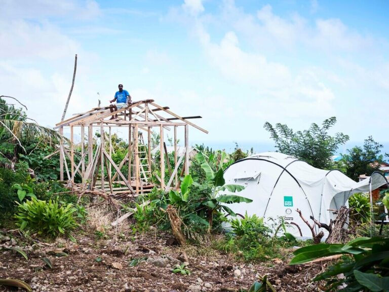 A man is building a permanent shelter in Dominica, next to his temporary ShelterBox tent.