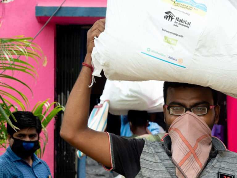 Man with covered nose and mouth, carrying ShelterBox aid on his head