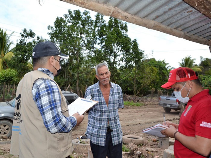 3 men talking, 2 of them in masks and taking notes