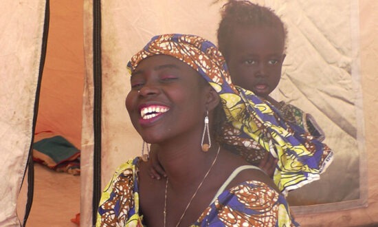 Woman smiling a camera with a baby in a carrier on her back