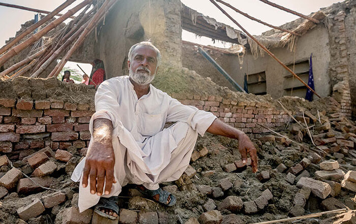 Man in Pakistan crouches outside his home destroyed by flooding