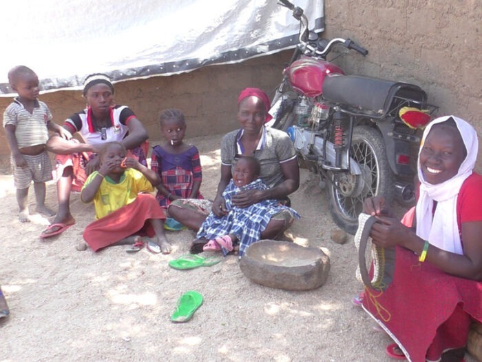 A woman sitting with her family, sewing a hat