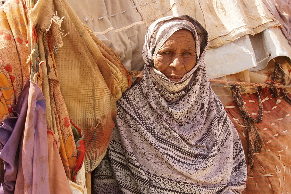Lady in head scarf sitting in front of different pieces of fabric