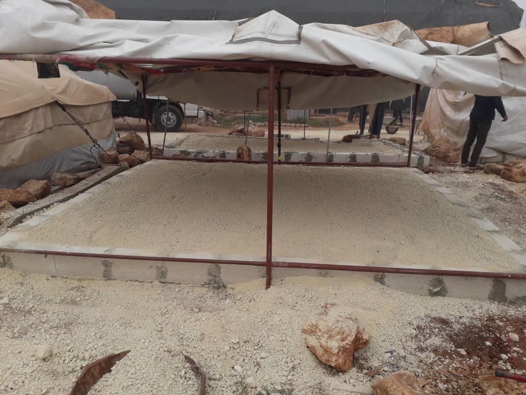 A square of bricks filled with concrete to create a level base, with tarpaulins above suspended on posts