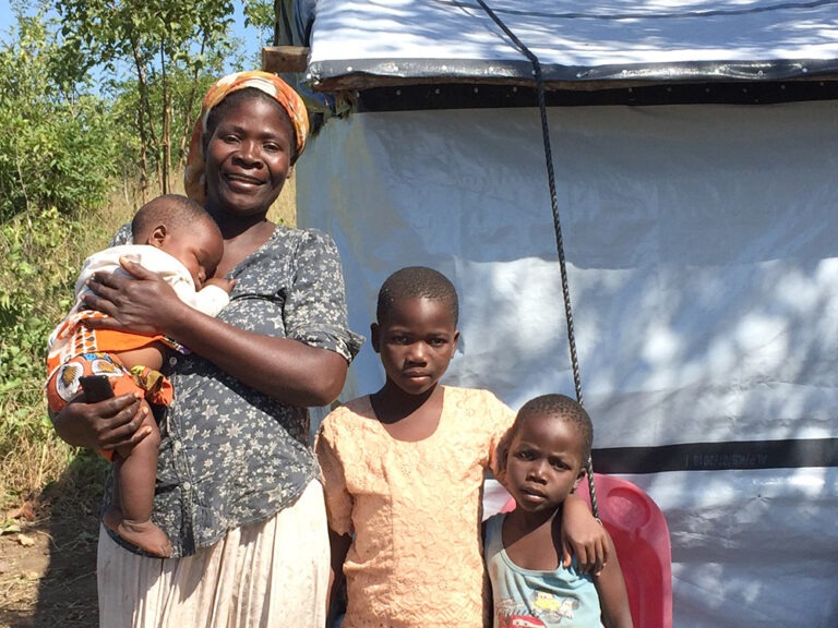 A mother and three children standing in front of a repaired shelter in Malawi