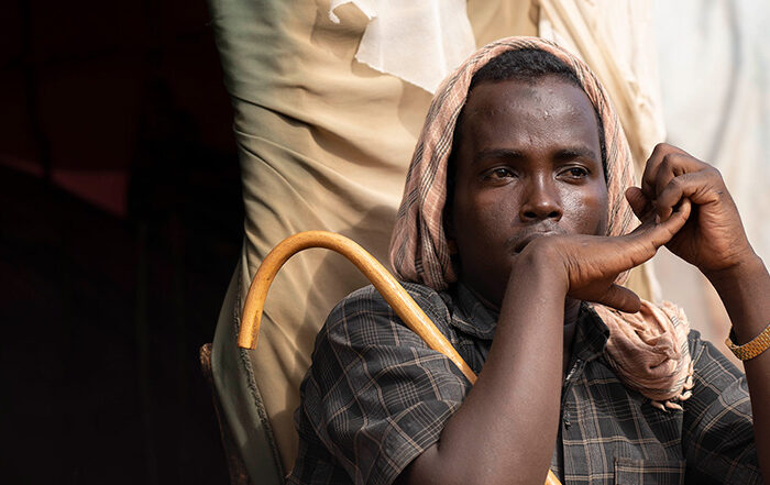 Photo of a man holding a stick sitting outside a tent