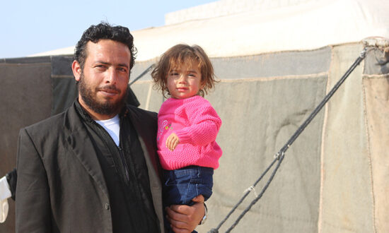 Man holding a child next to a tent in Syria