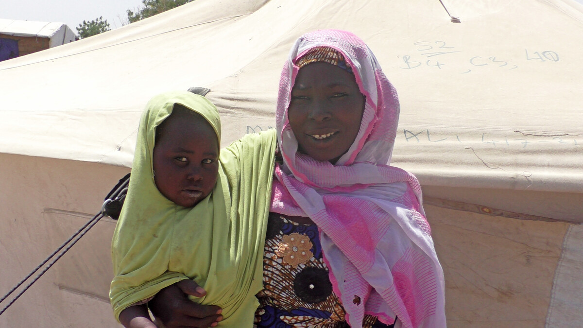 Woman holding a child outside a tent in Minawao Camp, Cameroon