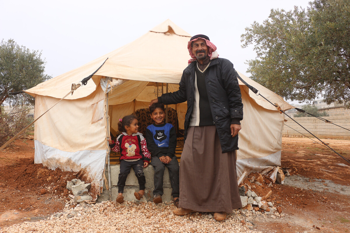 Man and two children standing outside a tent in Syria