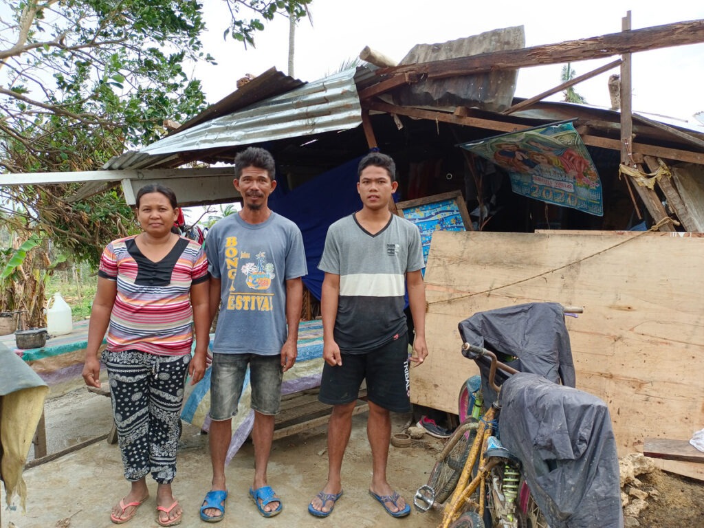 A woman and two men standing in front of a makeshift shelter