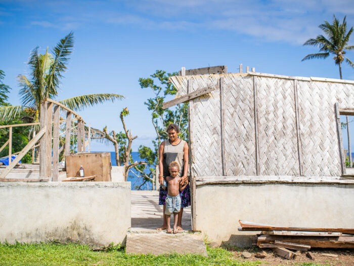A woman and a child stand in front of a makeshift shelter in Vanuatu