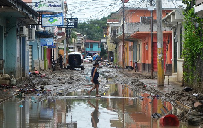 Woman walking through flooded street between damaged buildings in Honduras